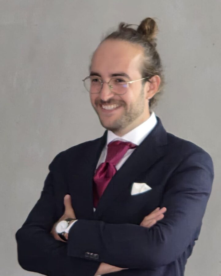 Pierre Guichard in a dark suit and red tie, arms folded and smiling, at his thesis defence.